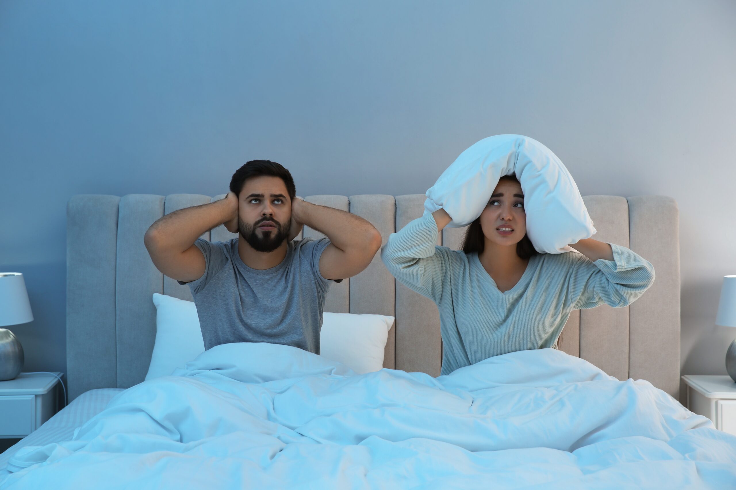 Two people in bed, unable to sleep due to noisy neighbours
