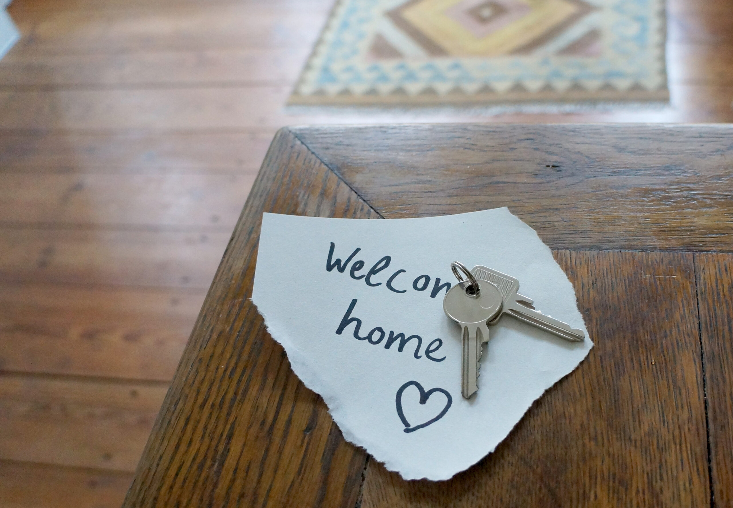 A note on a table saying welcome home with some keys placed on top of it.