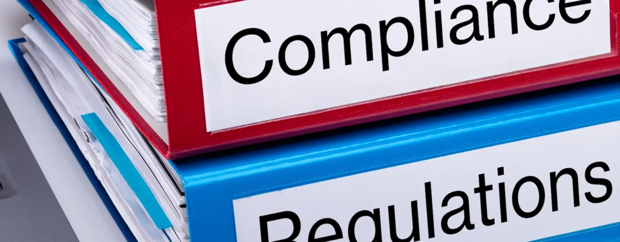 One blue folder titled regulation stacked on a red folder titled compliance