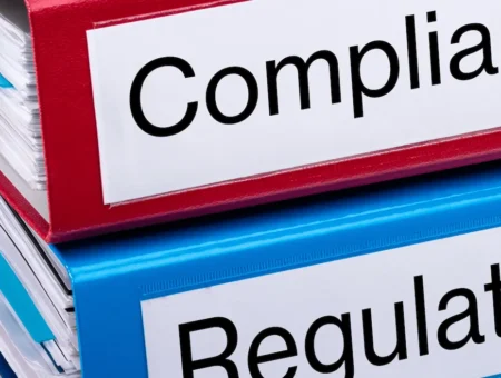 One blue folder titled regulation stacked on a red folder titled compliance