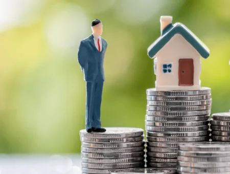 Two model people standing next to a model house with coins