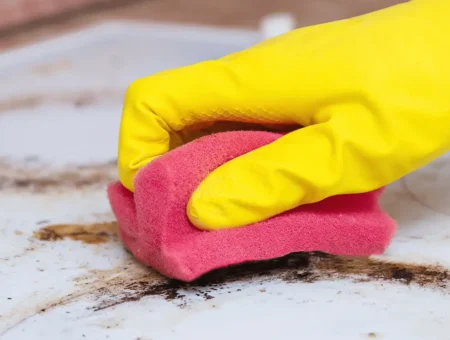 A person wearing yellow rubber gloves cleaning a dirty hob with a pink sponge