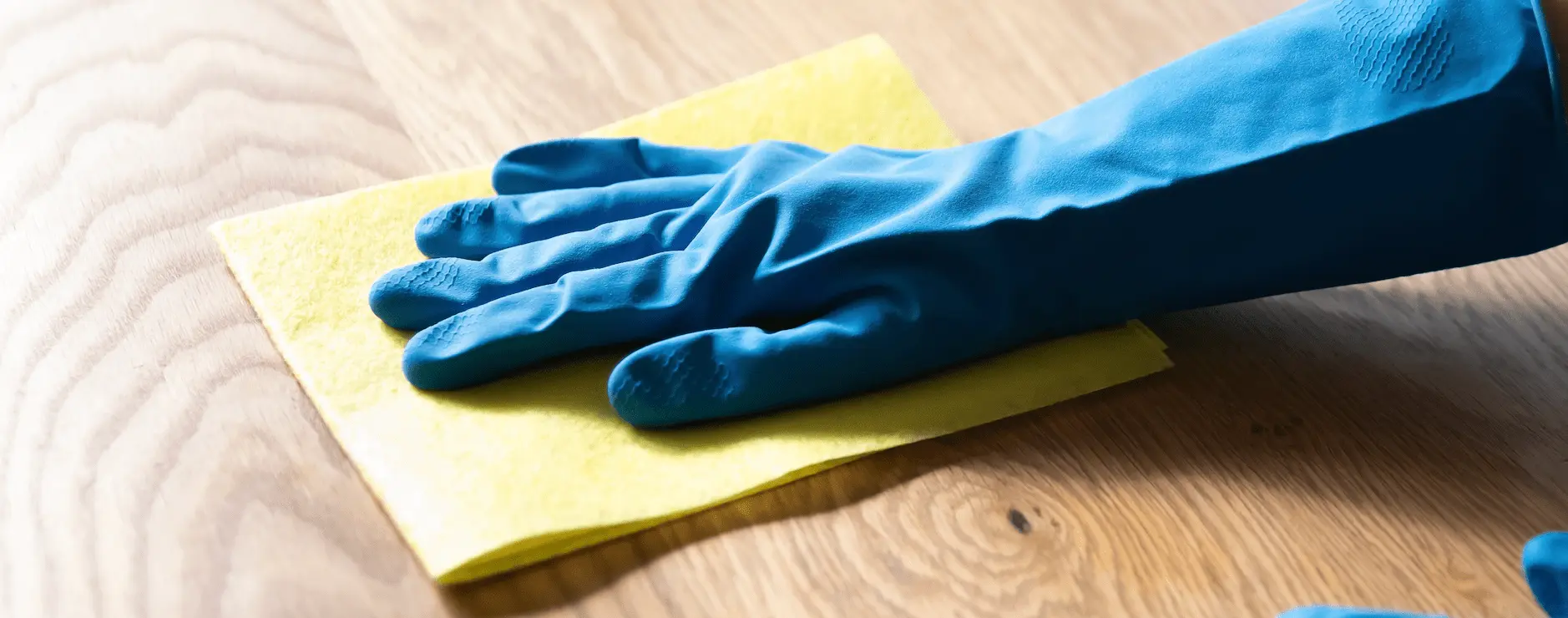 A person using blue rubber gloves and a yellow cloth to clean a worktop