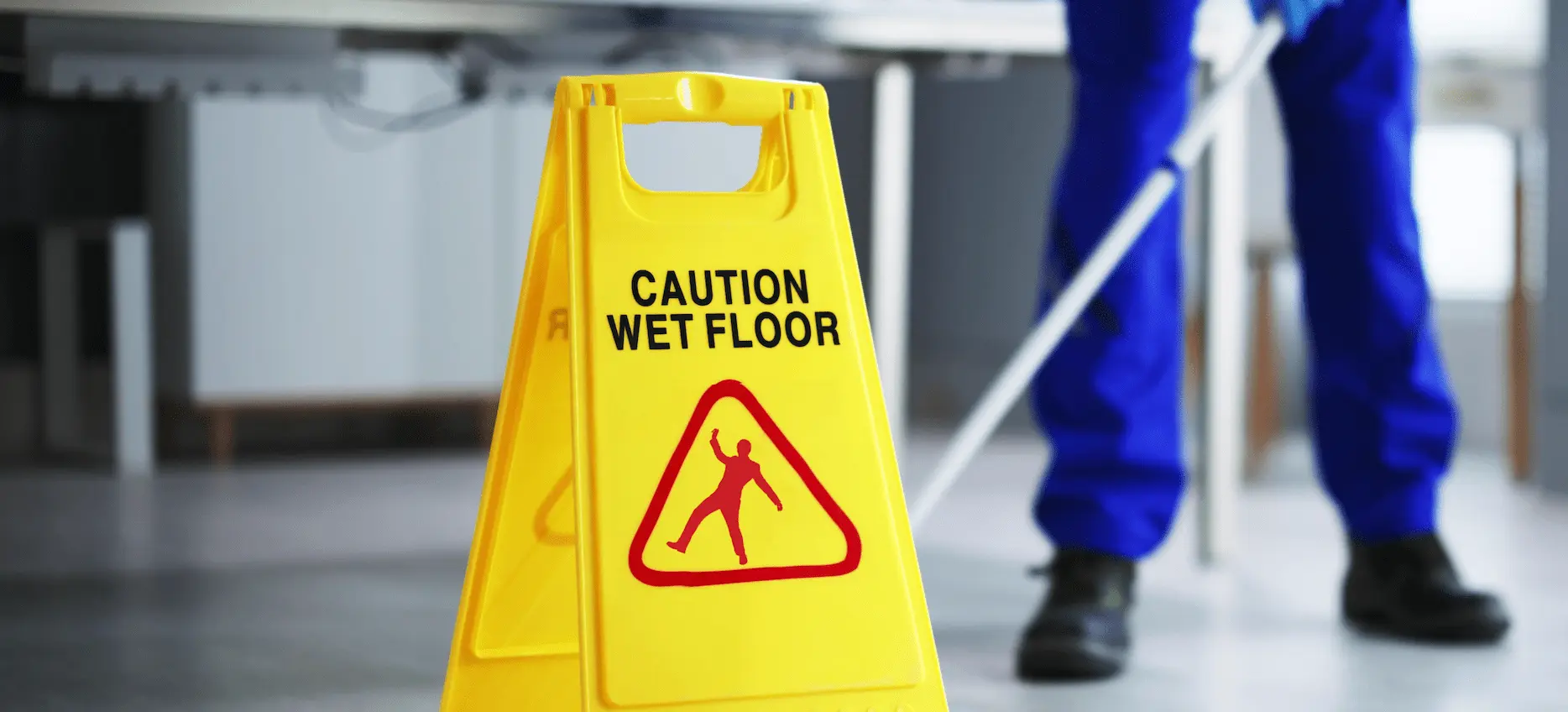 A janitor mopping the floor with a yellow wet floor caution sign
