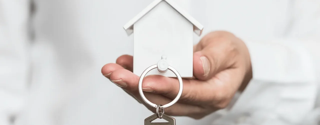 A person holding a white model house which doubles up as a keyring
