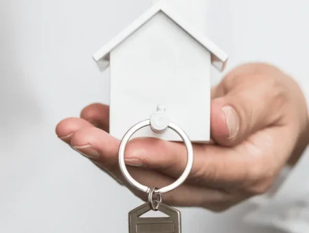 A person holding a white model house which doubles up as a keyring