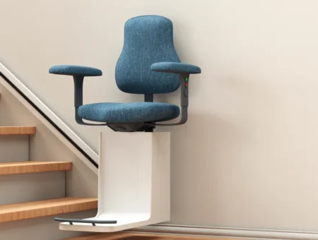 A stairlift with a blue chair, going up a wooden staircase