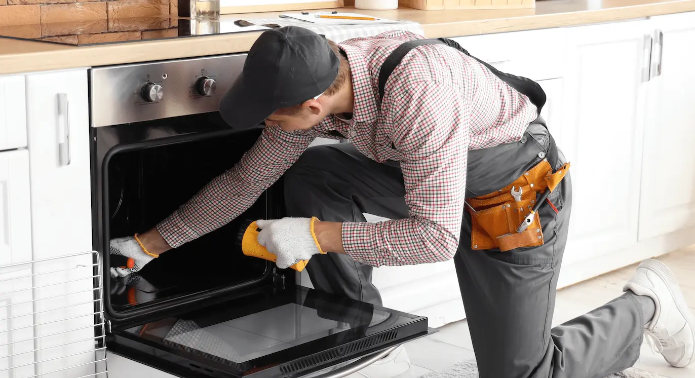 A worker fixing an oven in a rental property kitchen