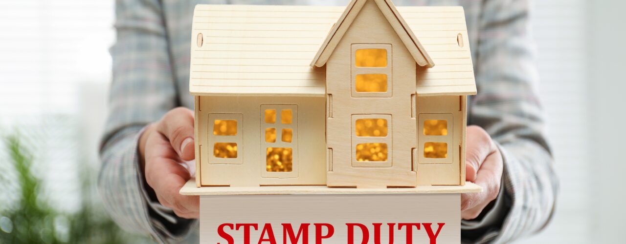 A person carrying a wooden model house with a sign that says 'stamp duty'